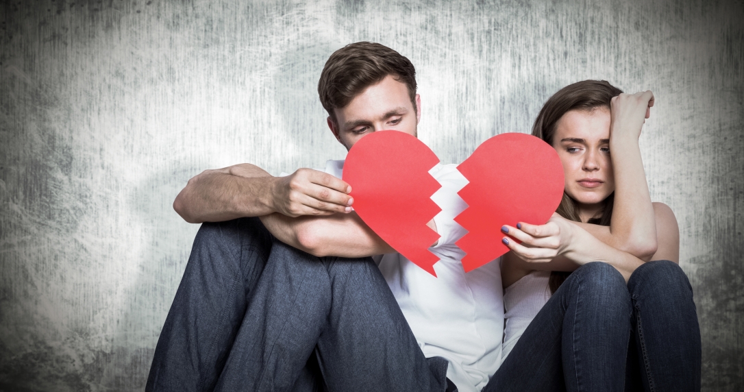 Young couple holding broken heart against grey background